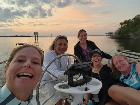 Group of five people smiling on a boat at sunset with calm water.