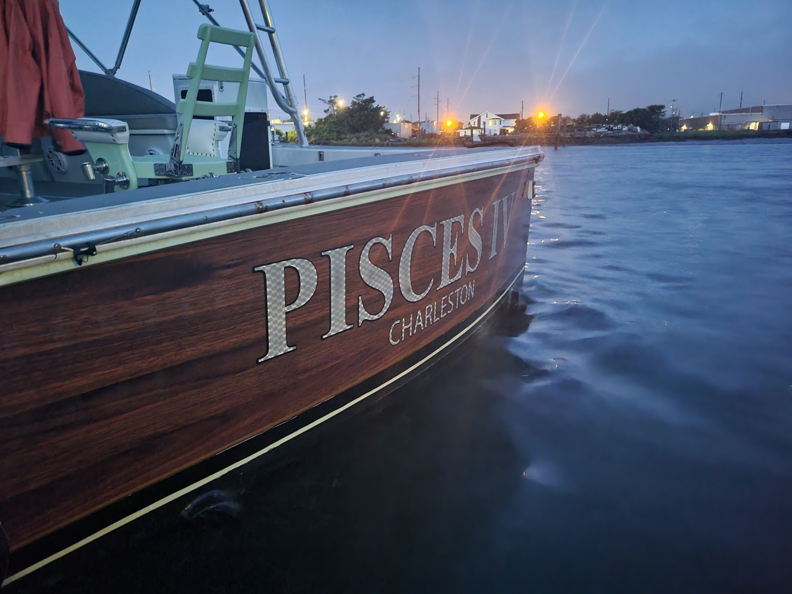 Boat named 'PISCES IV CHARLESTON' docked in calm water at dusk with distant lights.