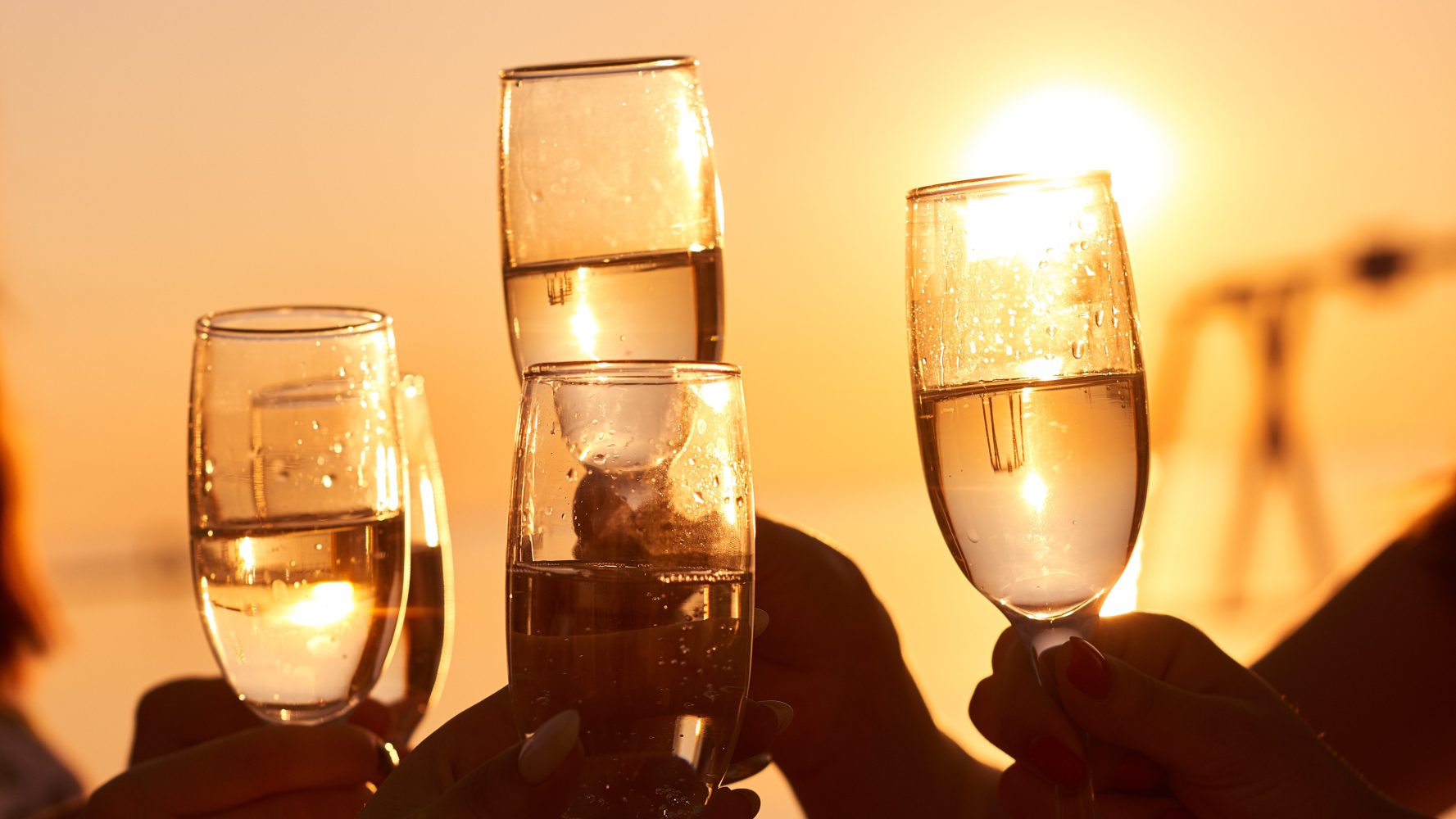 Four champagne glasses raised in a toast at sunset.