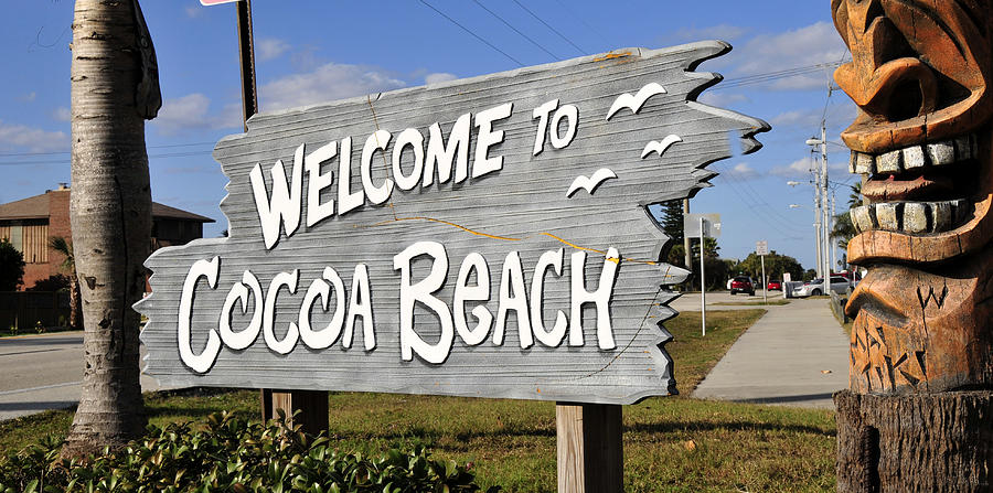 Sign reading 'Welcome to Cocoa Beach' with carved wooden tiki on the right.