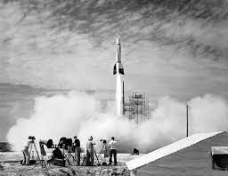 Black and white photo of a rocket launching, surrounded by smoke and photographers.