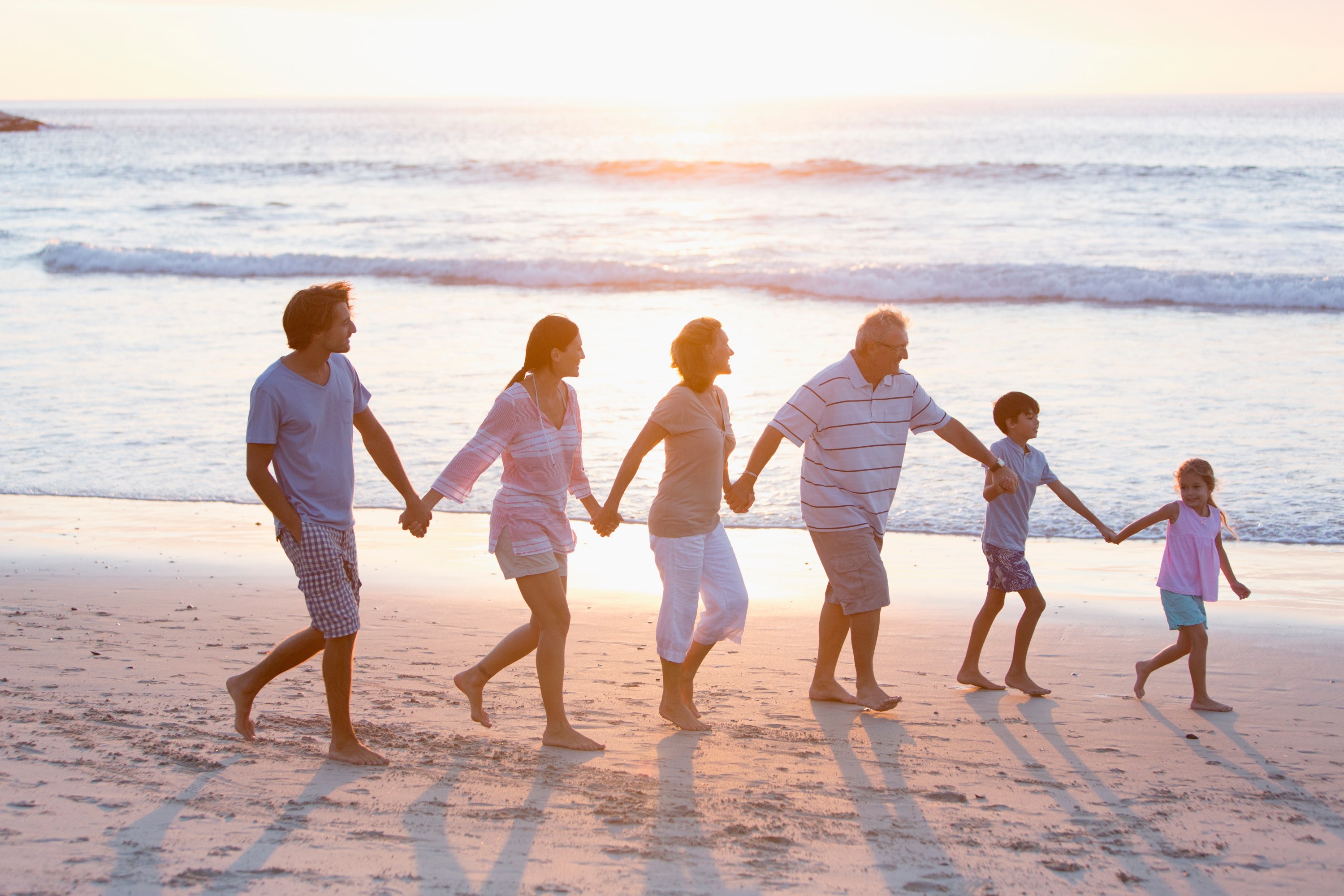 Family holding hands walking on the beach at sunset.