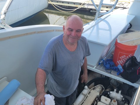 Man smiling on a boat by an engine, holding a white cloth.