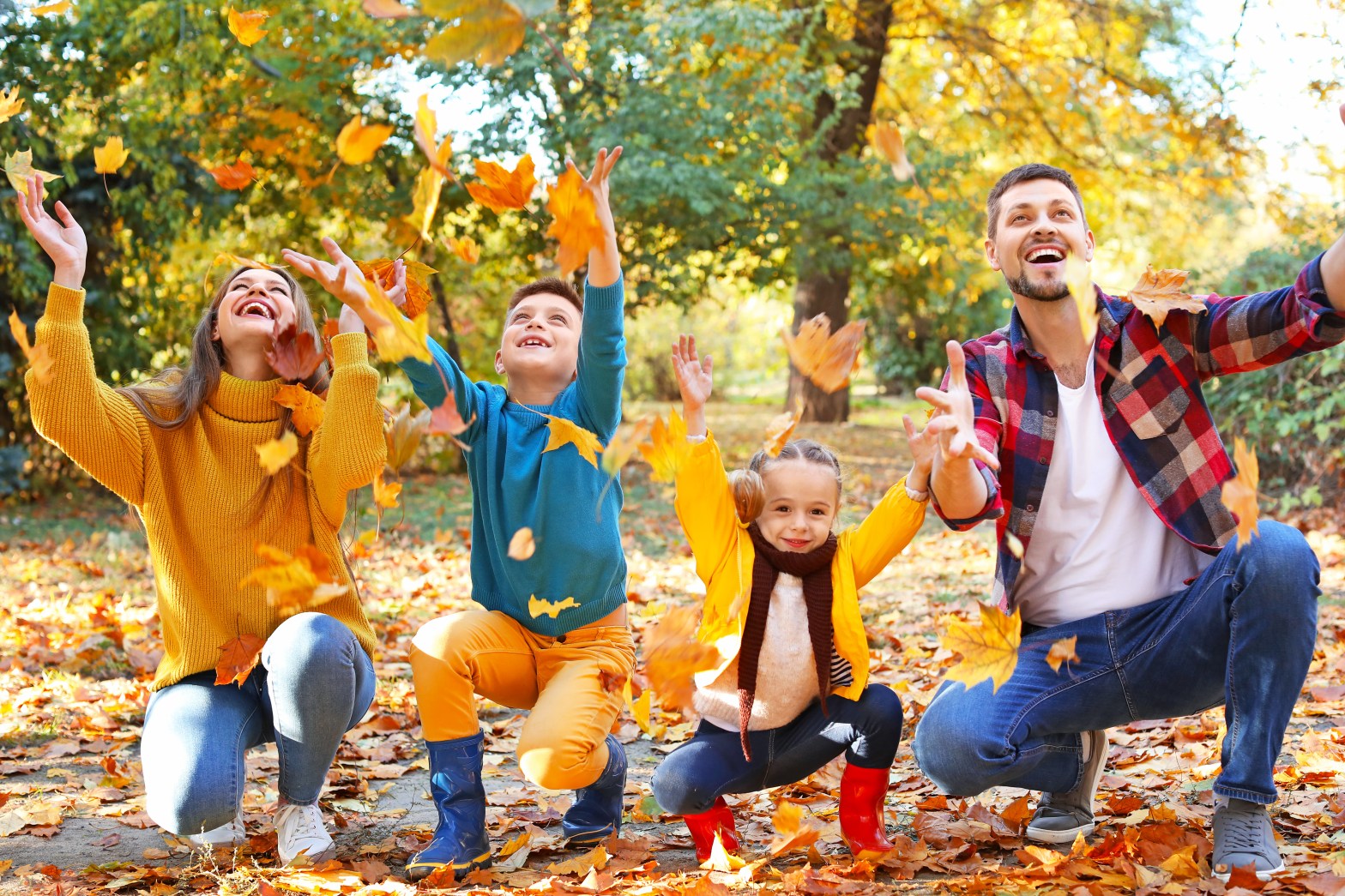 Family of four playing with autumn leaves in a park.