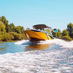Yellow speedboat cruising on a river under clear blue sky, surrounded by trees.