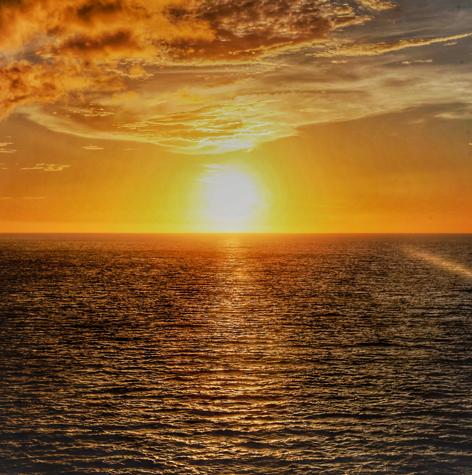 Sunset over the ocean with orange sky and rippling water.