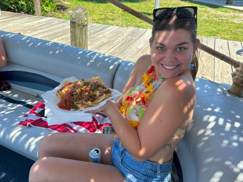 Smiling woman in lei holding nachos on a boat with wood deck background.