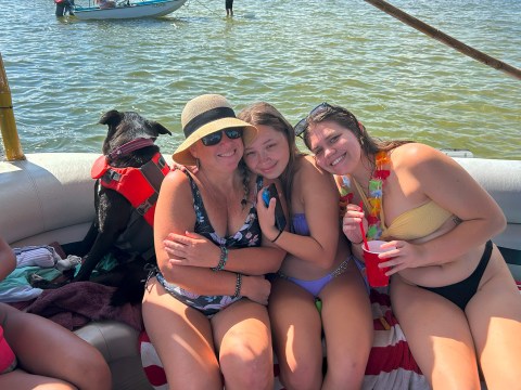 Three women and a dog on a boat; two boats visible in the water.
