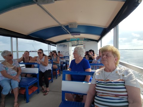 People sitting on benches under a covered boat roof, cruising on a calm body of water.