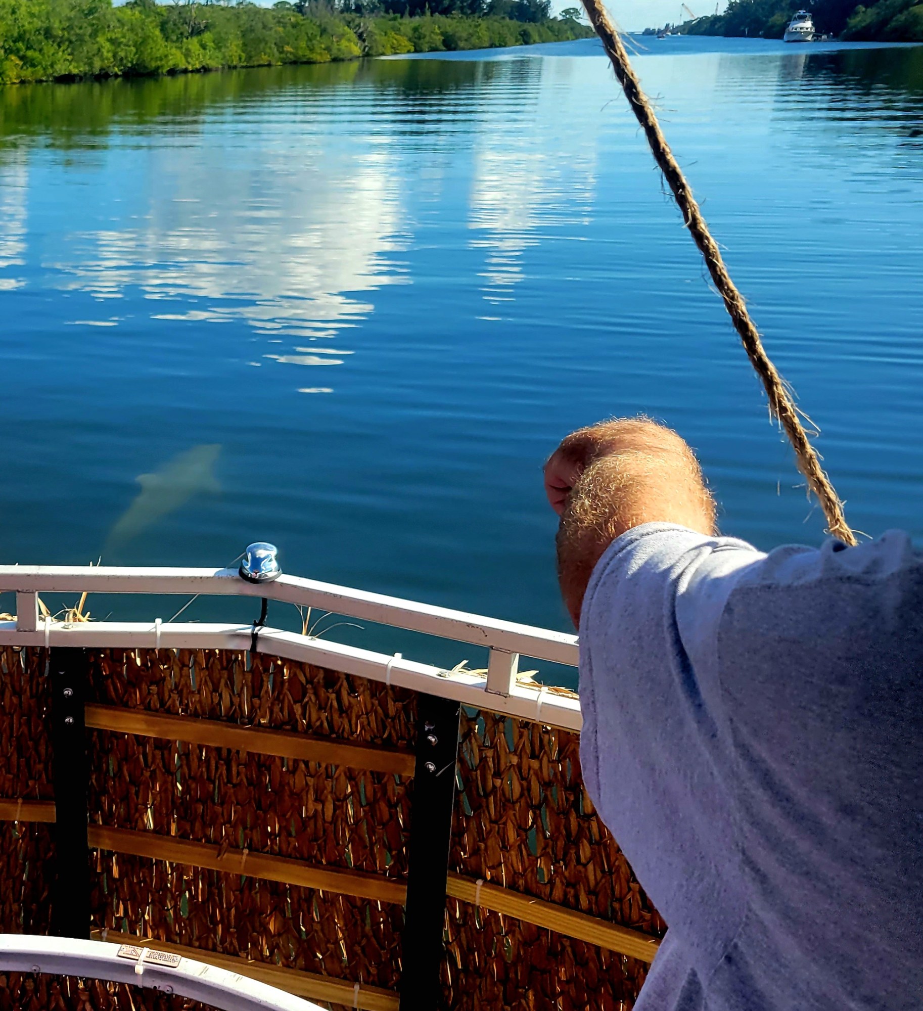 Person on a boat steering on a calm river under a blue sky with clouds.