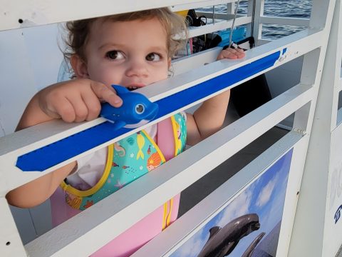 Child in a colorful life jacket peeking over a boat railing with ocean view.