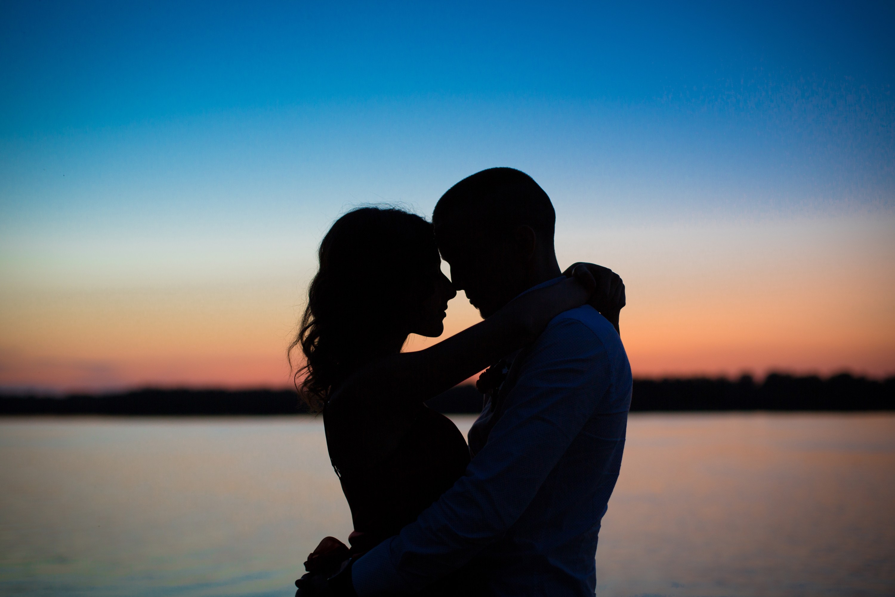Silhouette of couple embracing at sunset by the water.