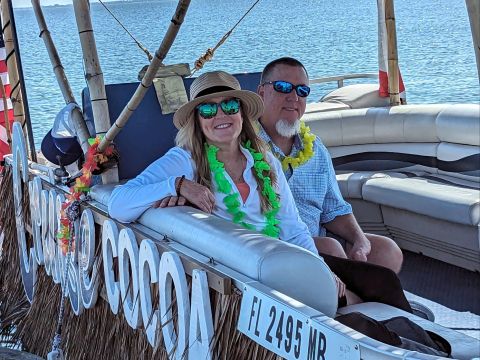 Couple wearing leis sitting on a tiki-style boat with a city skyline in the background.