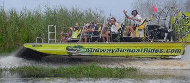Airboat with passengers waving while cruising through marshy water.