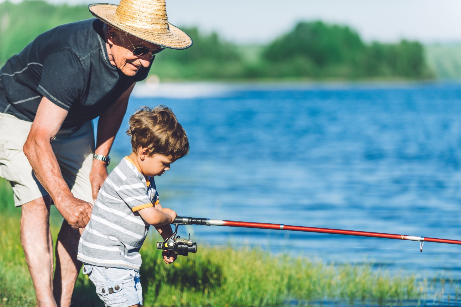 Older man and young child fishing by a lake on a sunny day.