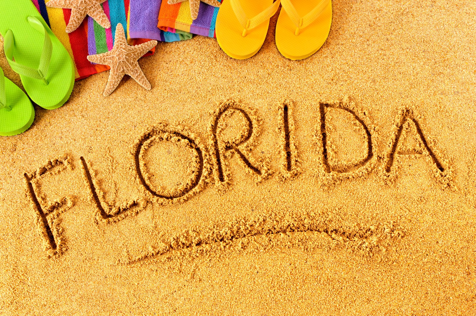 Sand with 'Florida' written, surrounded by flip-flops, towels, and starfish.