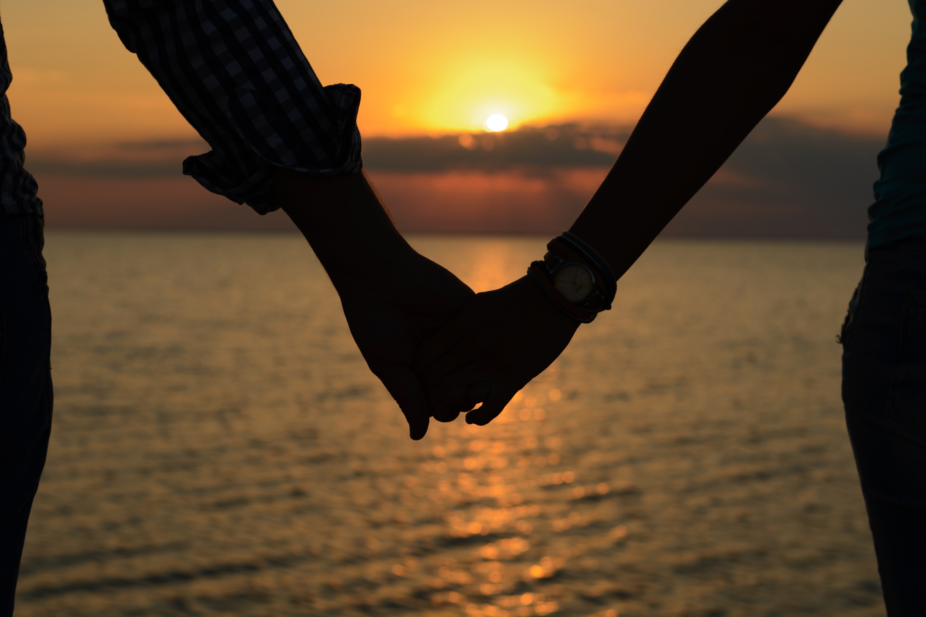Two people holding hands at sunset by the sea.