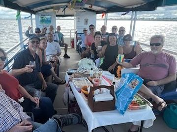 Group of people on a boat enjoying drinks and snacks, with water visible in the background.