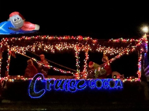 Christmas-lit boat with inflatable Santa riding a tube, text reads 'Cruise' in blue lights.
