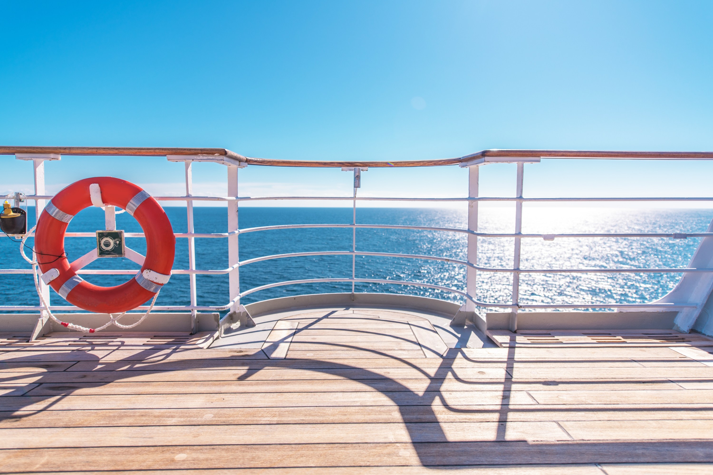 Sunny view of the ocean from a ship deck with a lifebuoy on the railing.