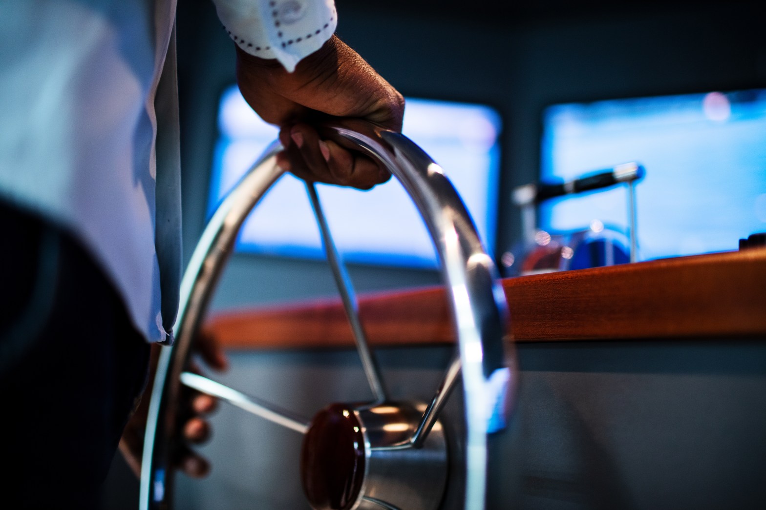 Person steering a boat with a metal wheel indoors.