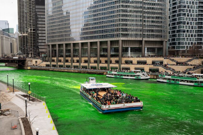 Boat on bright green river with people along the riverbank.