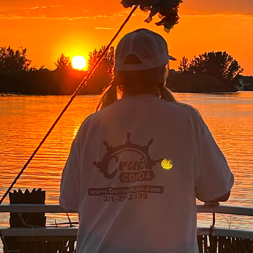 Person in a white shirt watching a sunset over a lake with silhouetted trees.