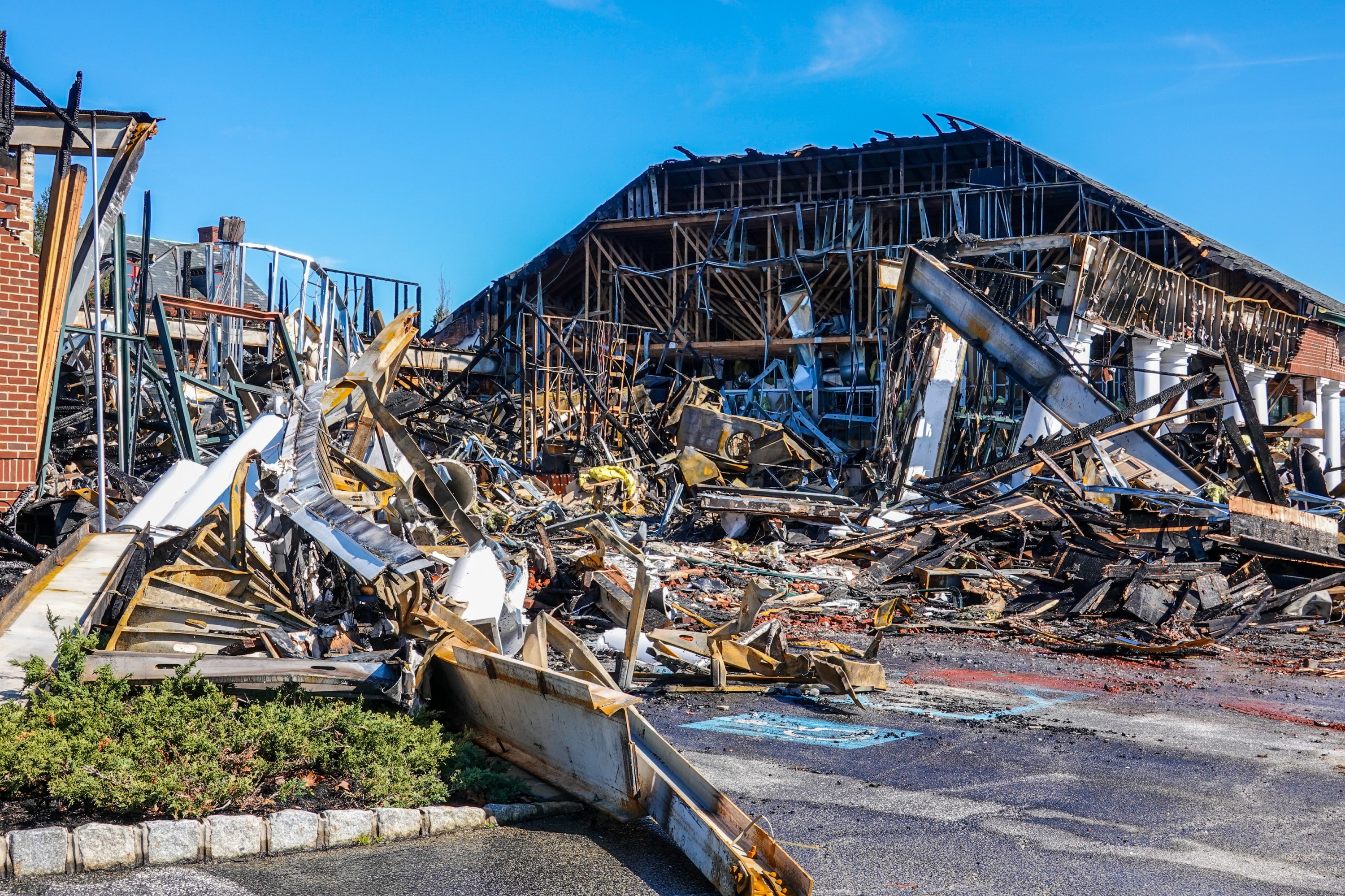 Building ruins with collapsed metal beams and debris under a clear blue sky.