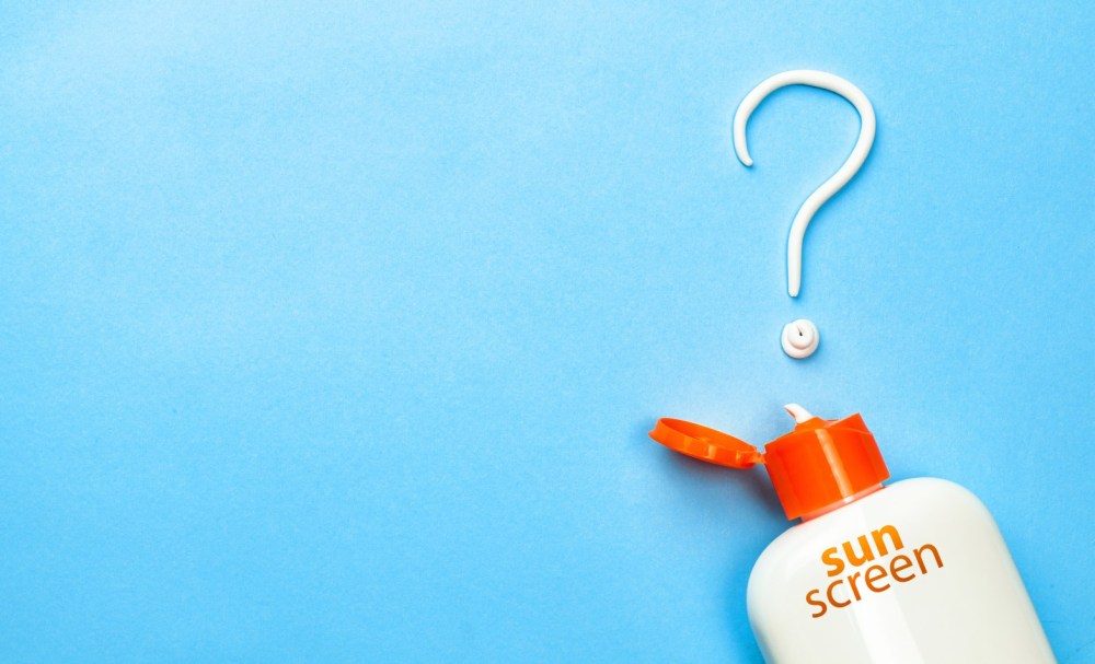 Sunscreen bottle with lotion forming a question mark on a blue background.