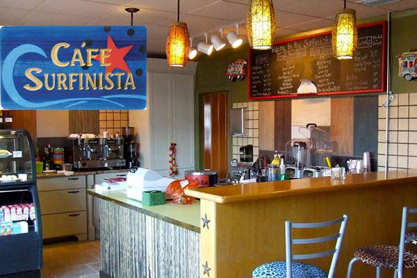 Cozy cafe interior with espresso machine, counter seating, and Café Surfinista sign.