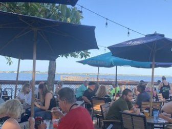 Outdoor restaurant with diners under umbrellas by the water.