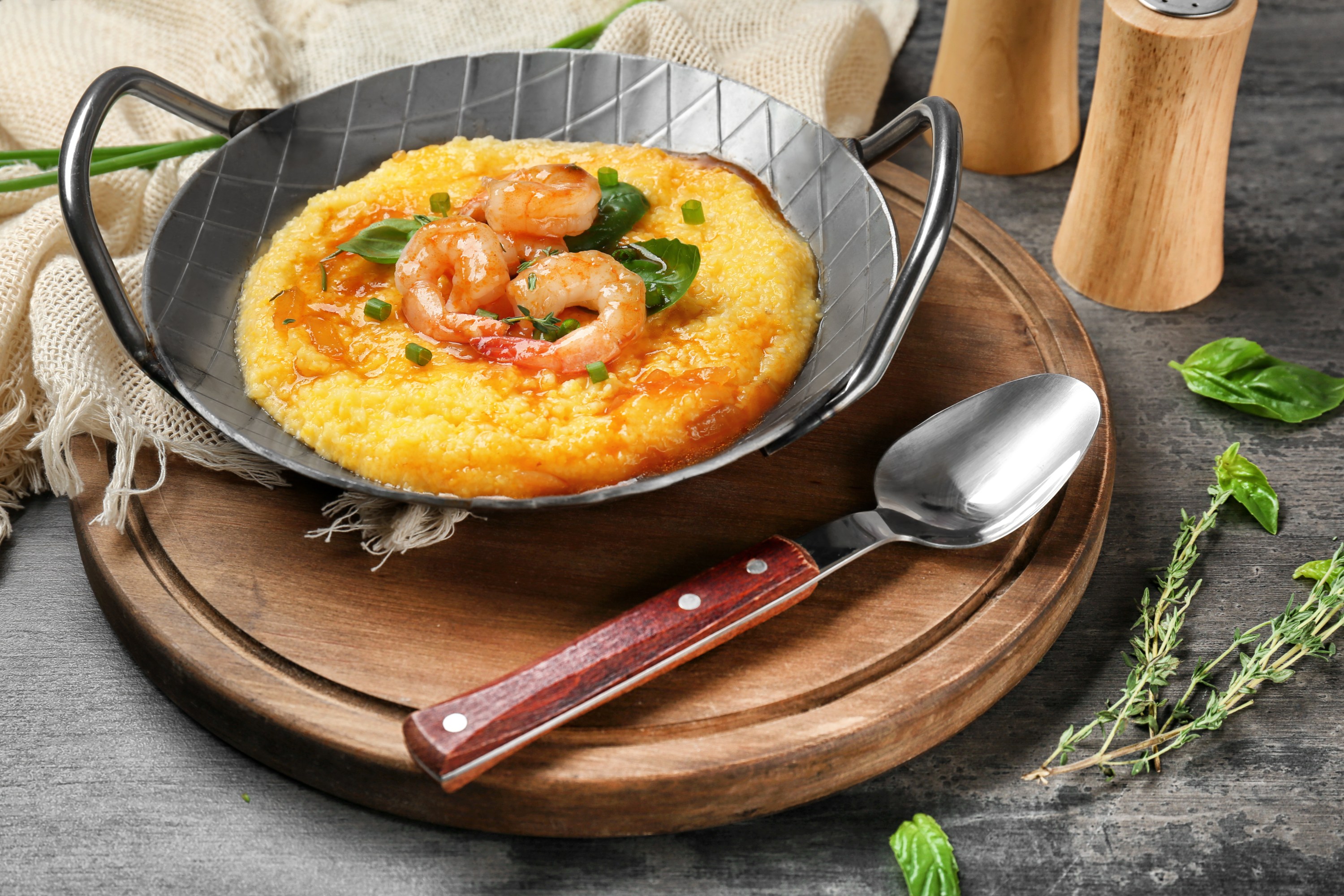 Shrimp and grits served in a metal dish with basil garnish on a wooden board.