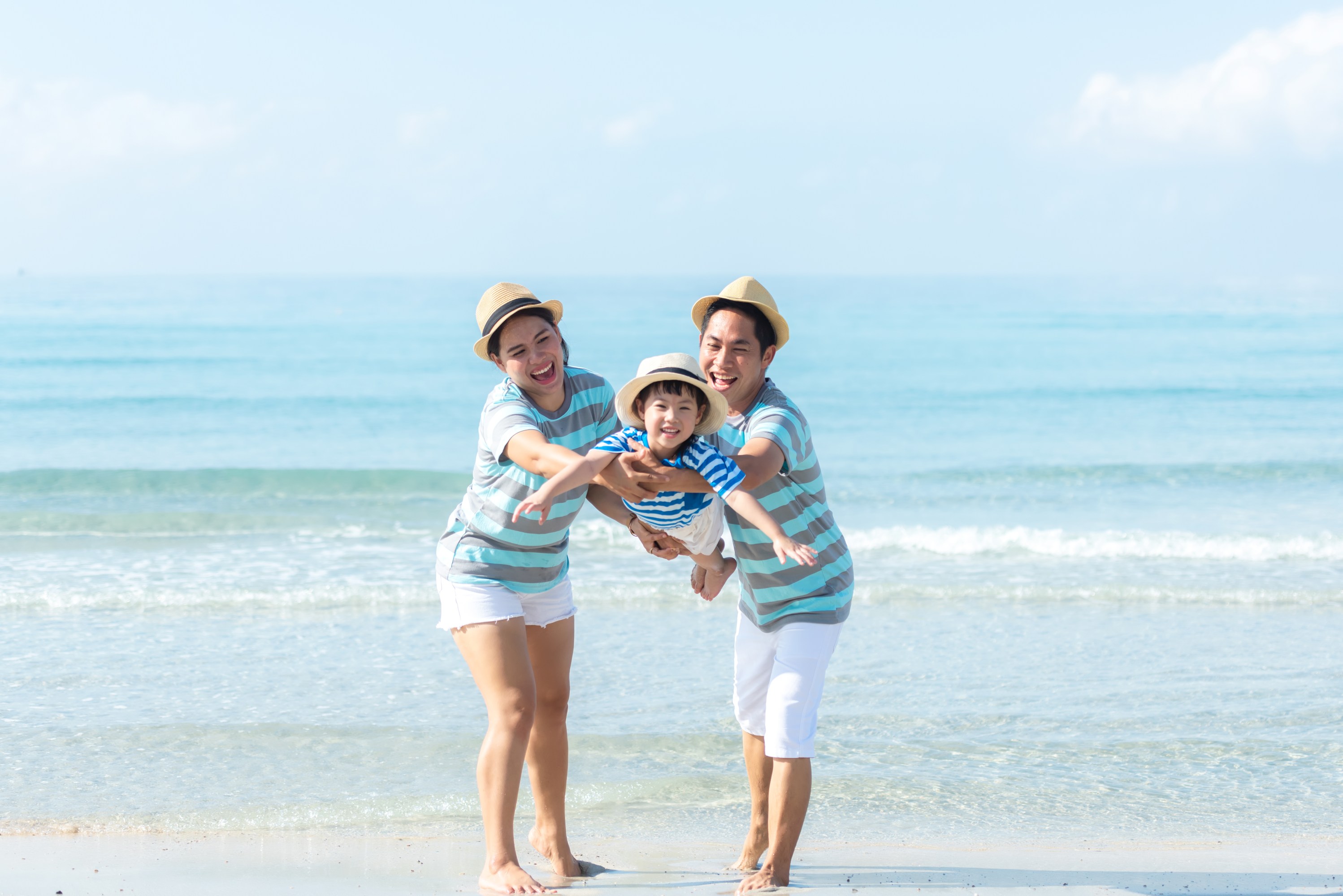 Smiling family in striped shirts playing on the beach by the sea.