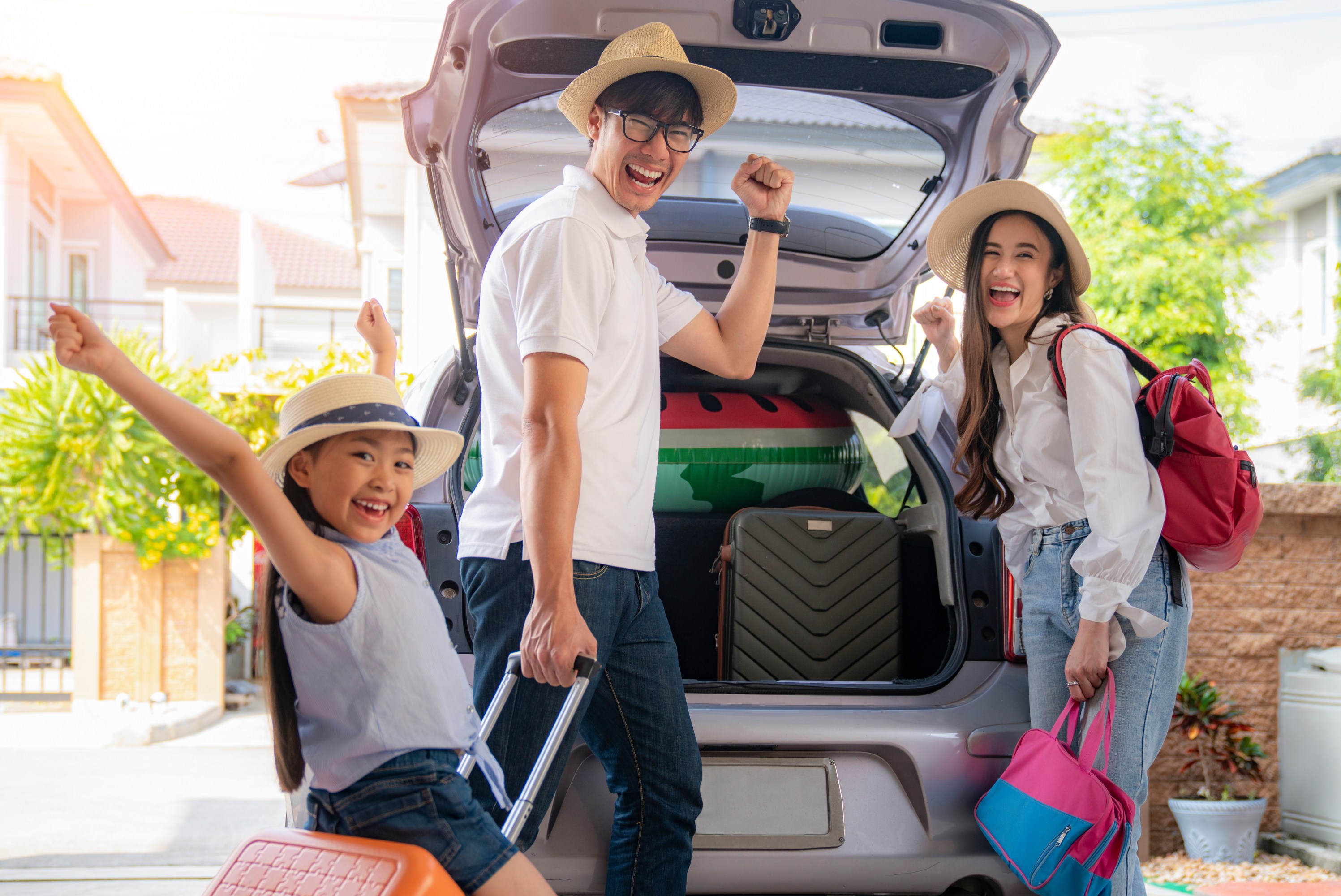 Family excitedly packing car trunk, holding suitcases and bags, ready for a trip.