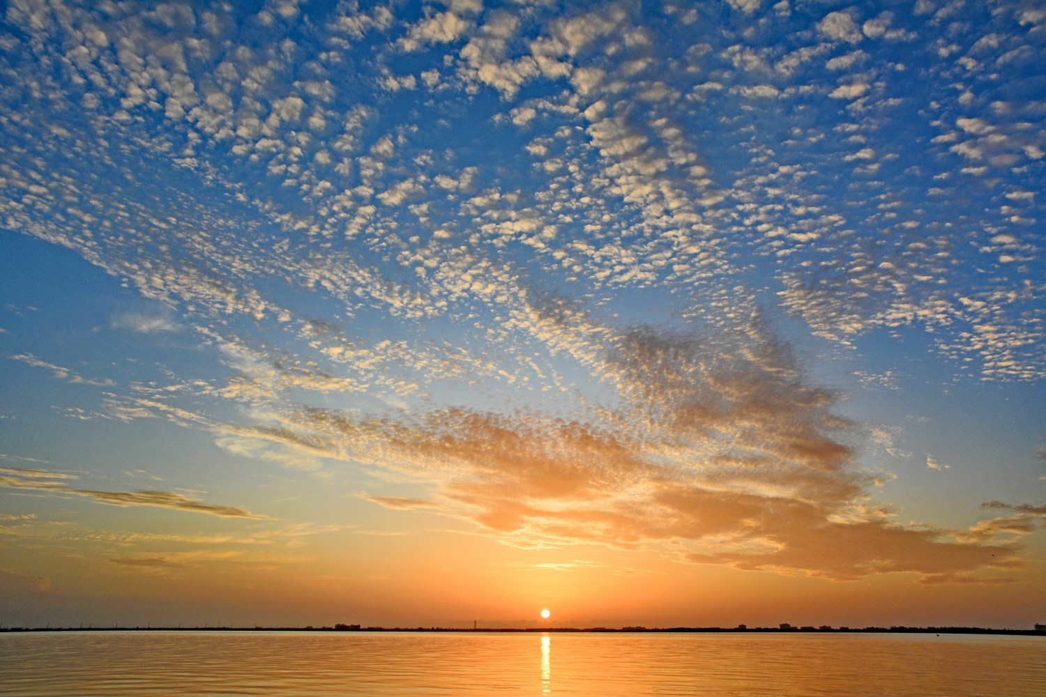 Vibrant sunset over water with scattered clouds in a blue and orange sky.