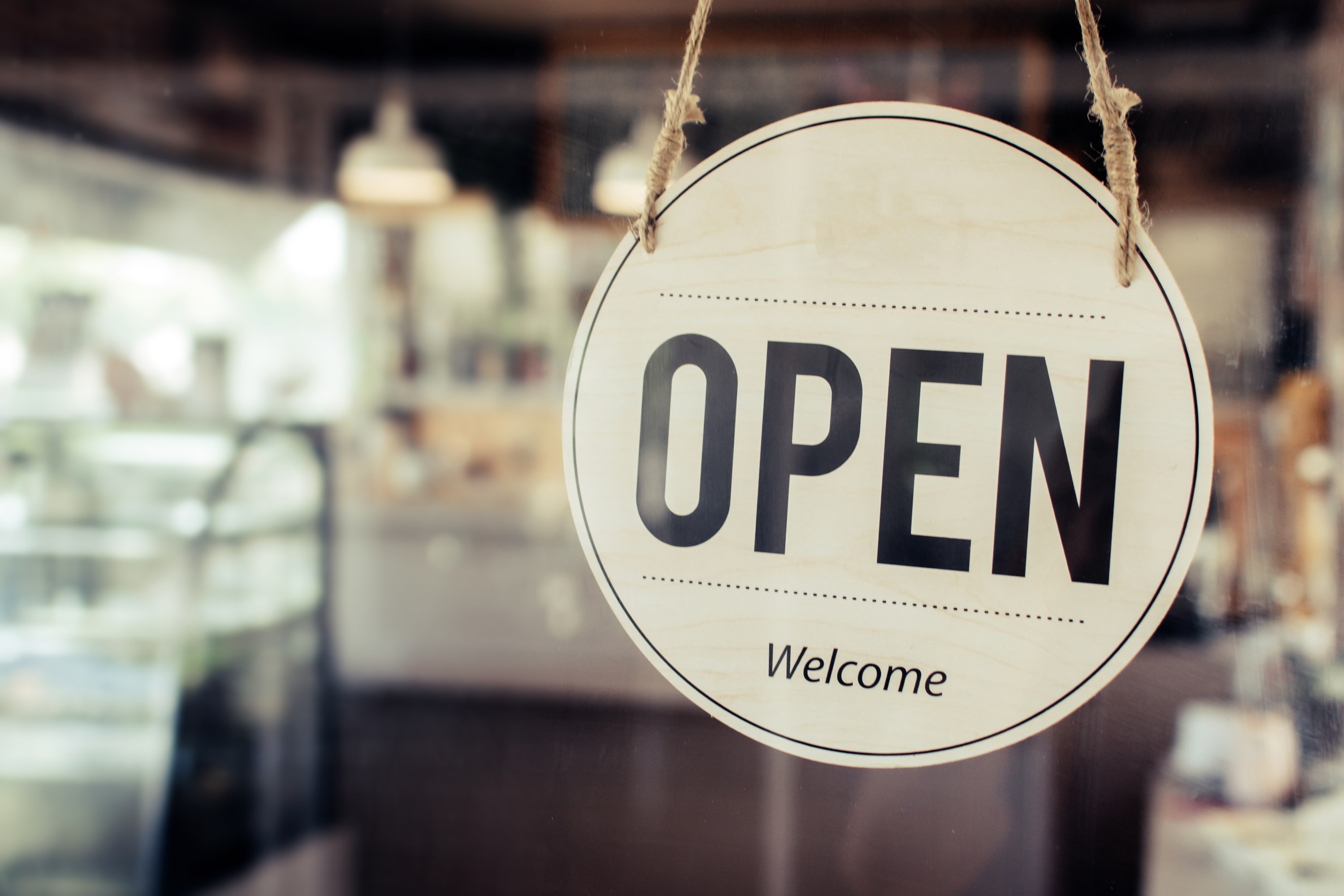 Round sign on glass door says 'OPEN Welcome' in a café setting.