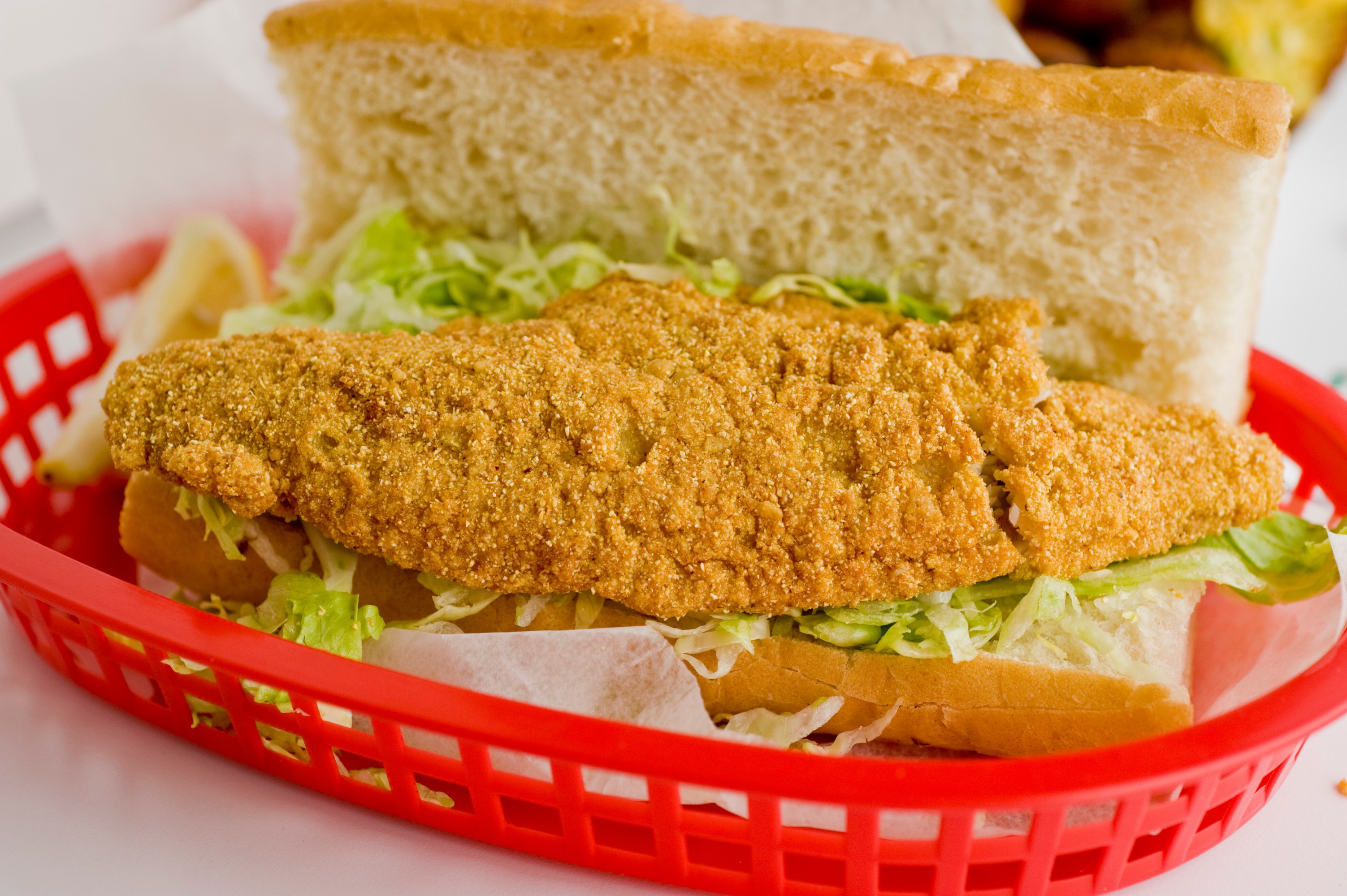 Fried fish sandwich with lettuce in a red basket lined with paper.