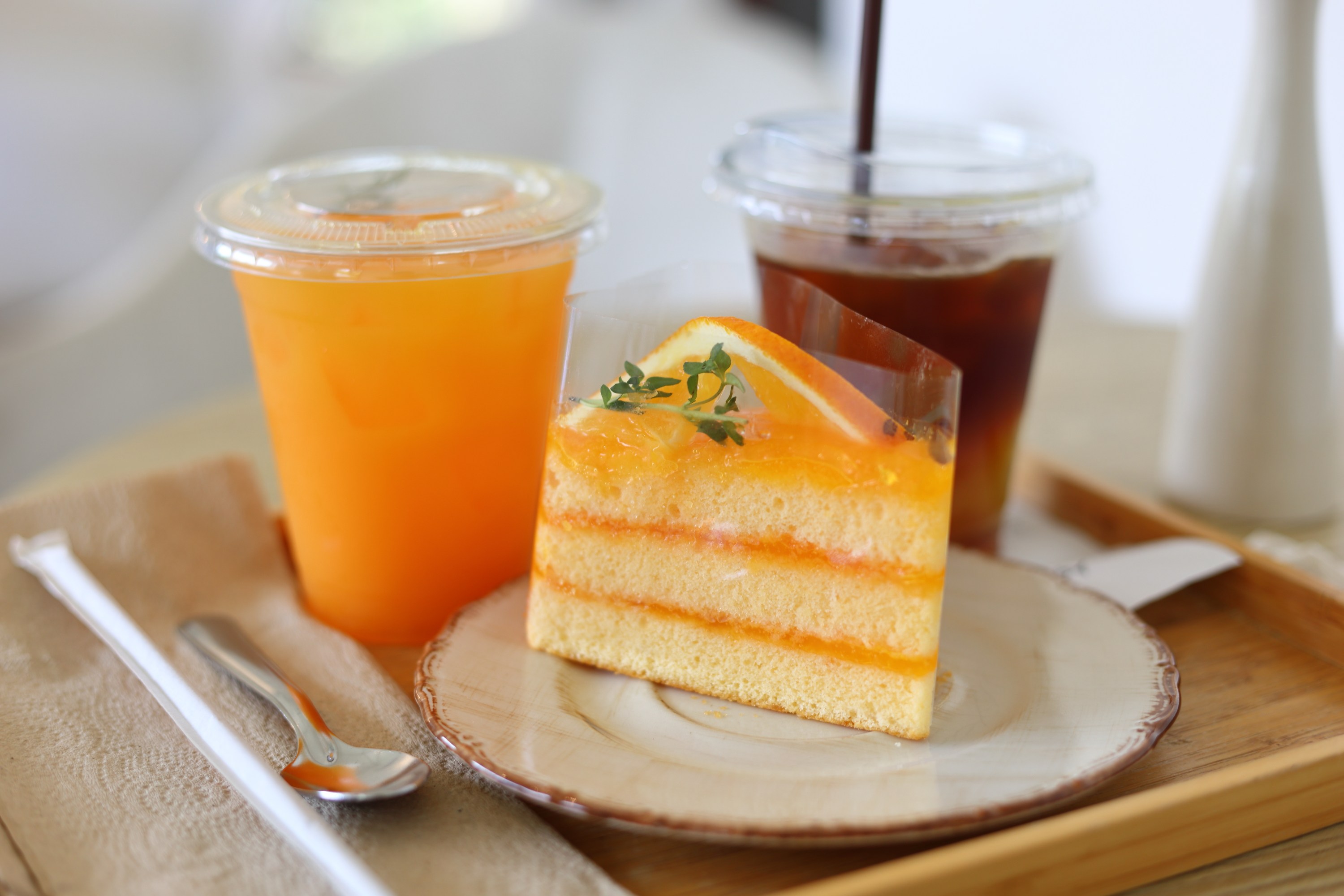 Slice of orange cake with iced drinks on a wooden tray.