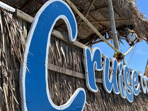 Large blue sign with 'Cruise' on straw hut with Florida flag.
