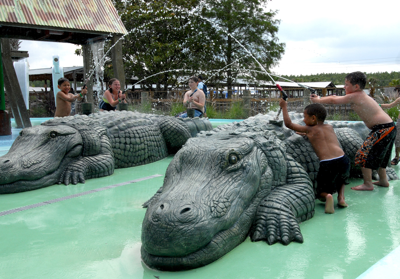 Children play on alligator-shaped water fountains at a splash park.