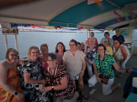 Group of people on a boat posing for a photo with a river and bridge in the background.