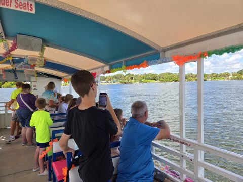 People on a decorated boat looking at a scenic lake view with trees.