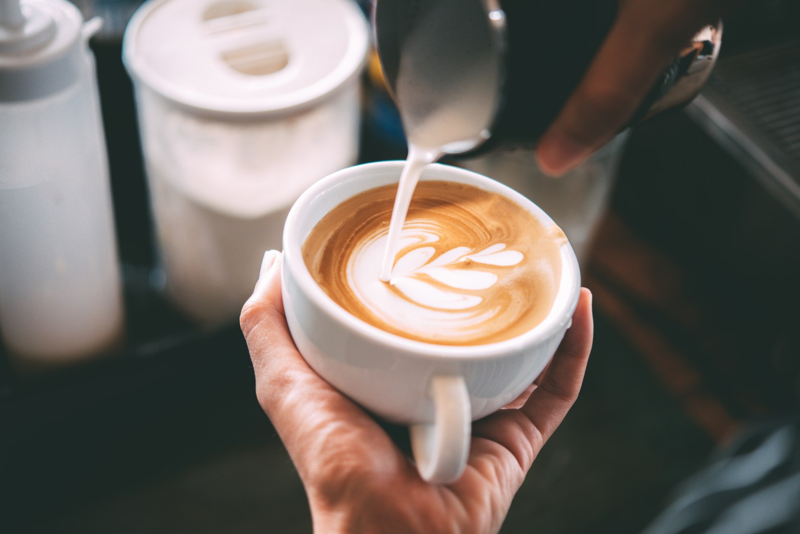 Person pouring milk to create latte art in a cup.