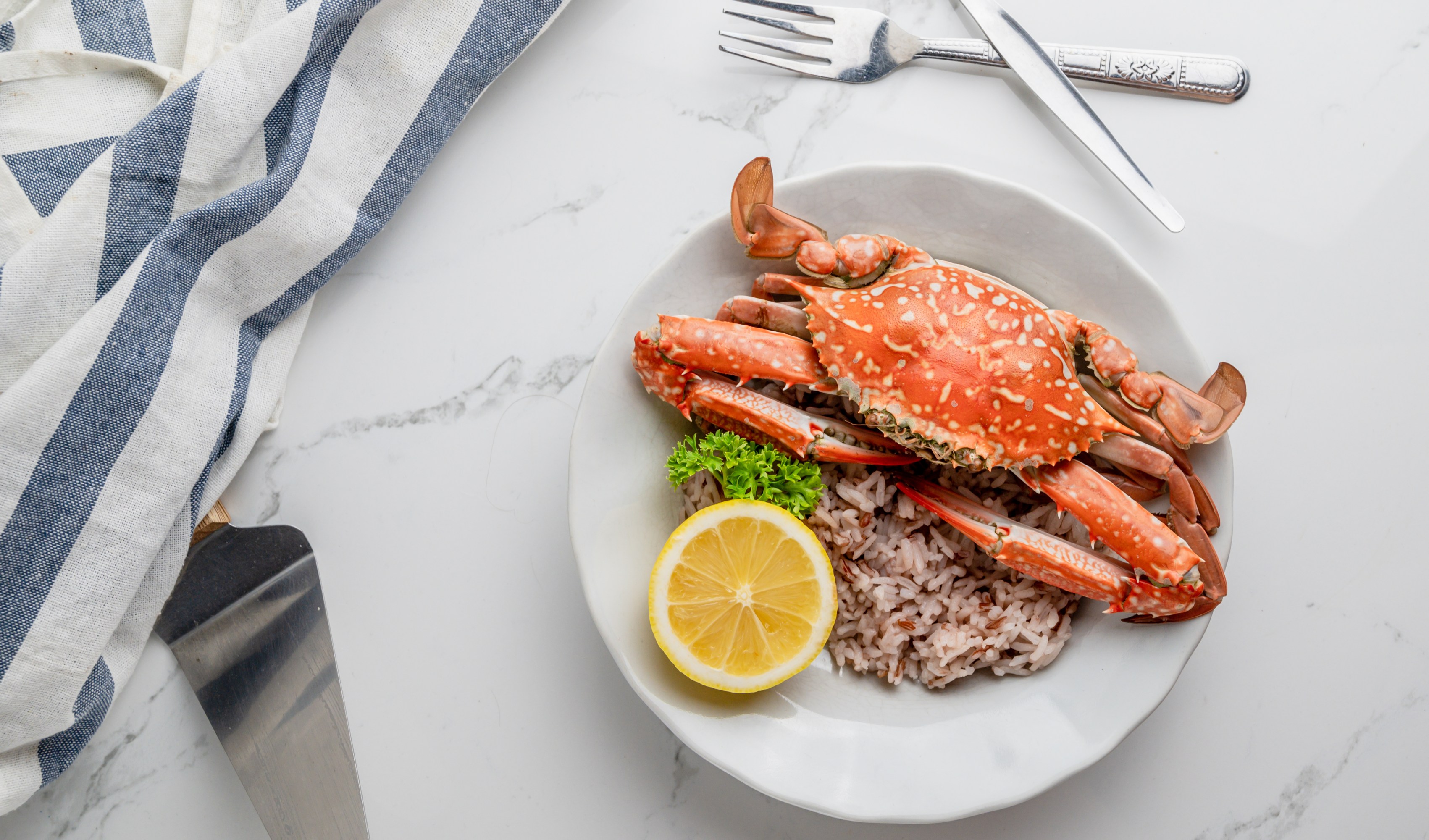 Crab on rice with lemon slice and parsley, fork and knife on side.
