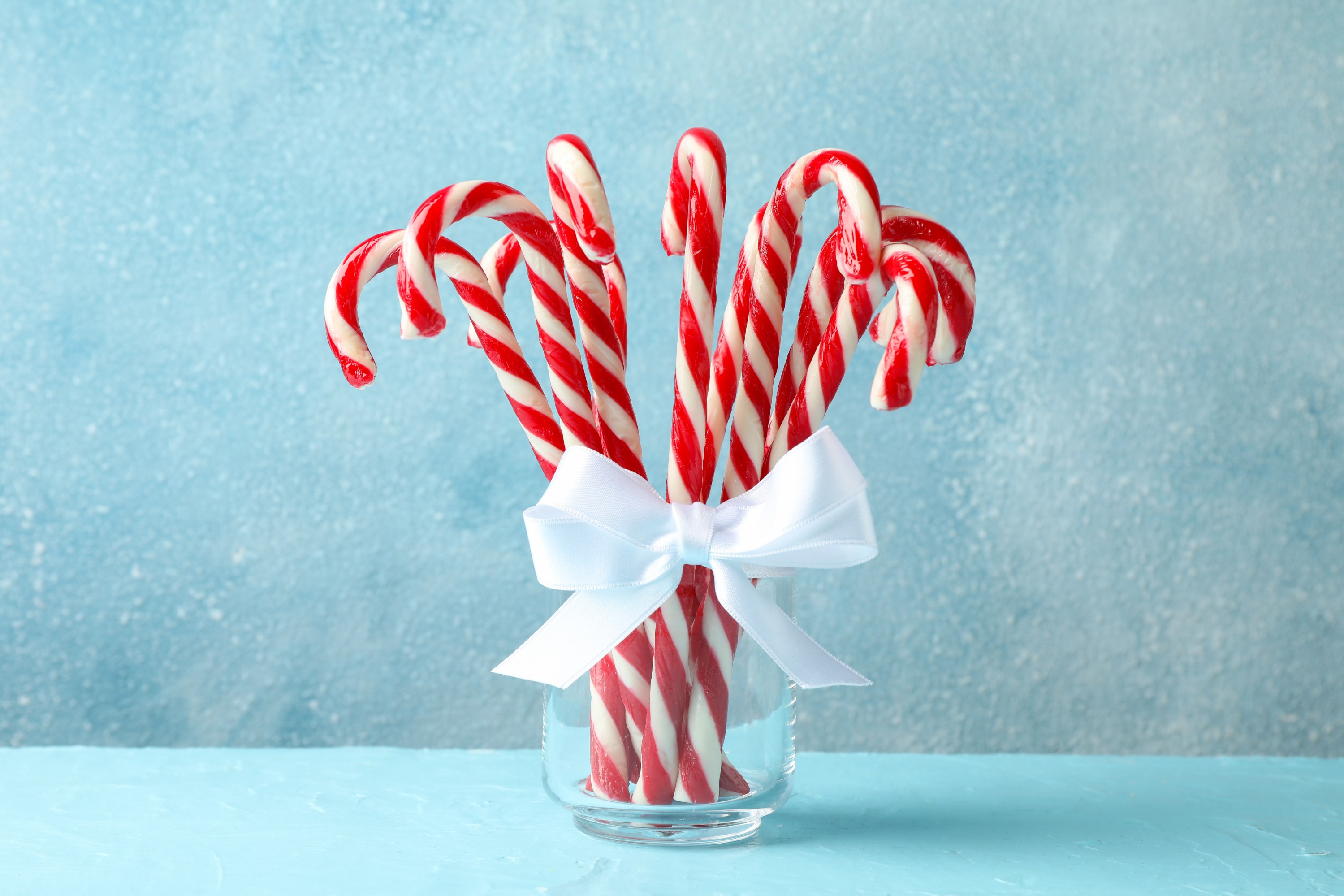 Jar of red and white candy canes tied with a white ribbon on a blue background.