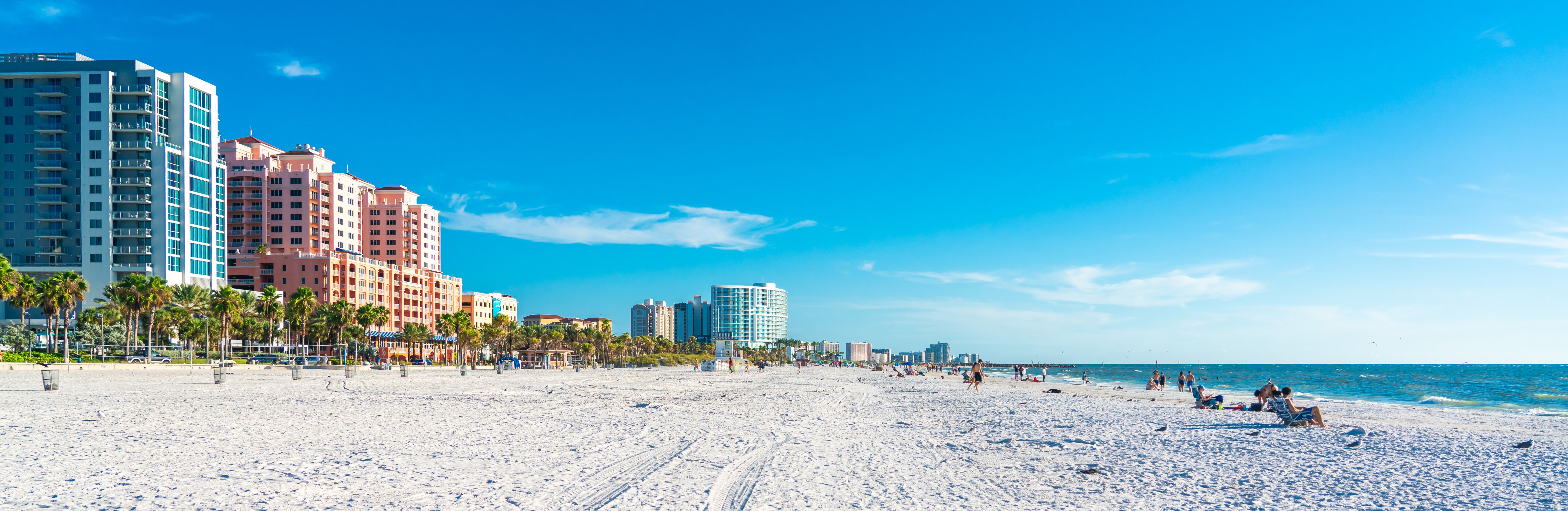 Beachfront with tall buildings, people sunbathing, and a clear blue sky.