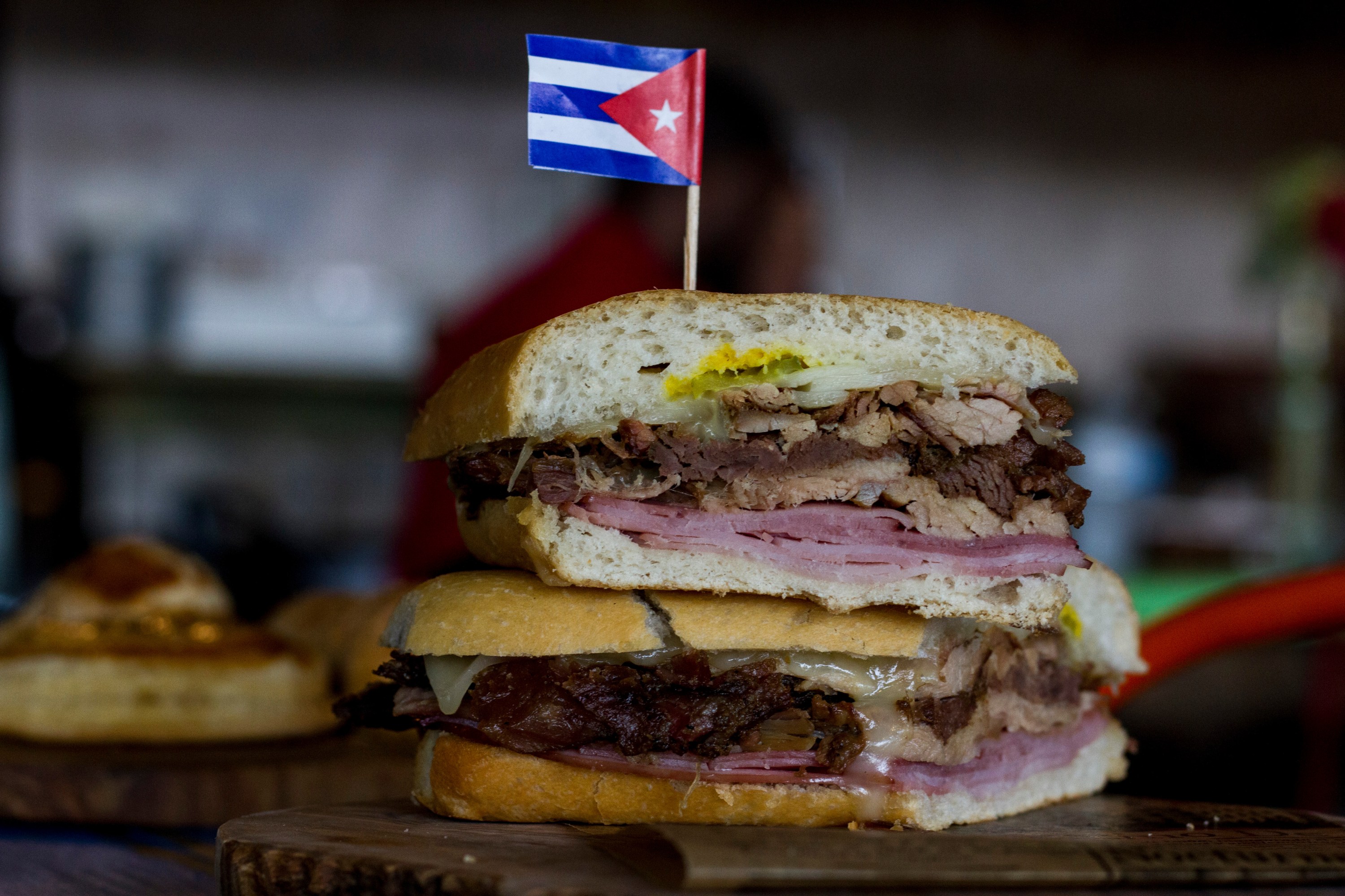 A Cuban sandwich with ham and pork, topped with a Cuban flag on a toothpick.
