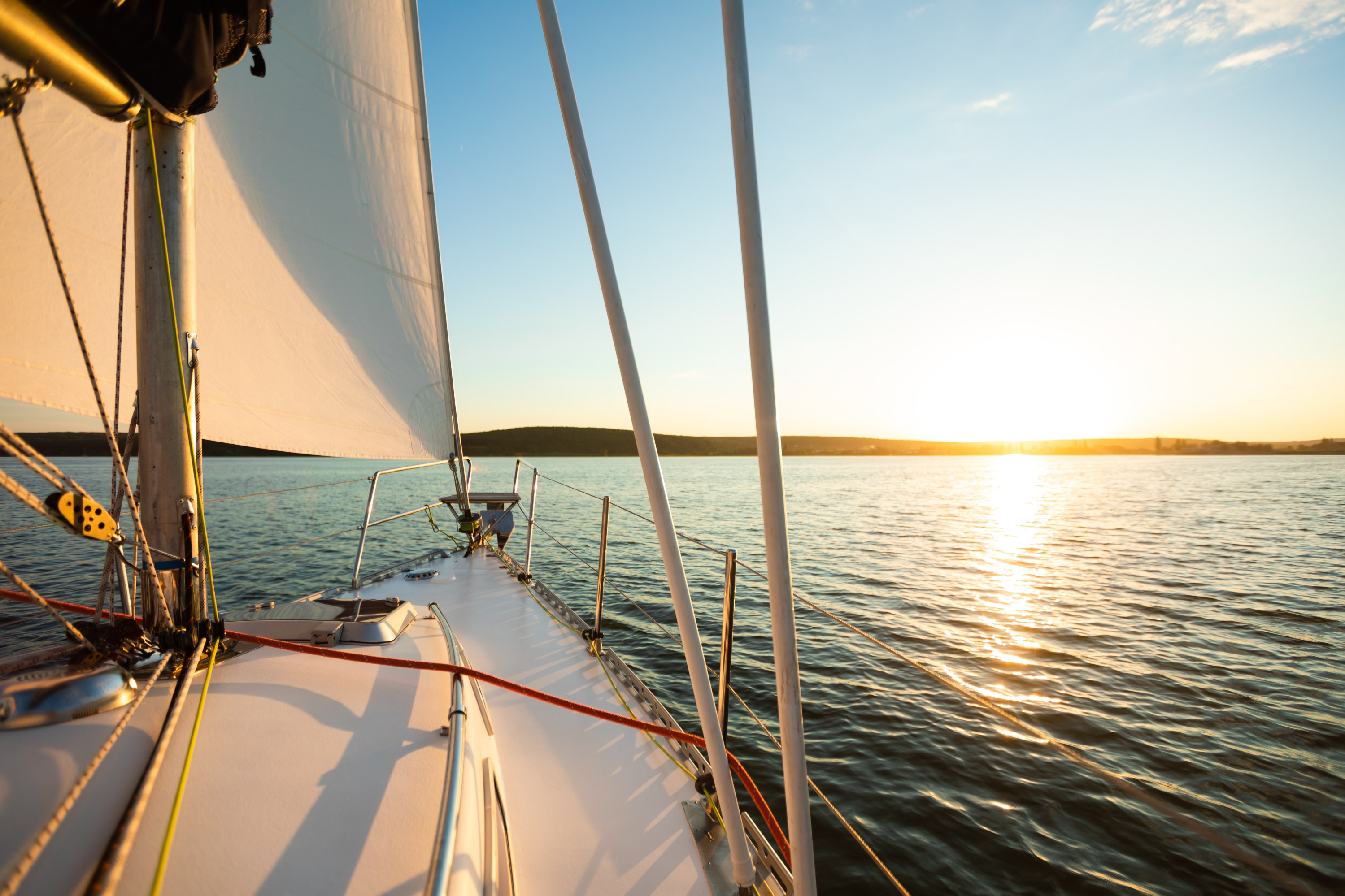 Sailing boat on calm waters at sunset with visible sails and horizon.