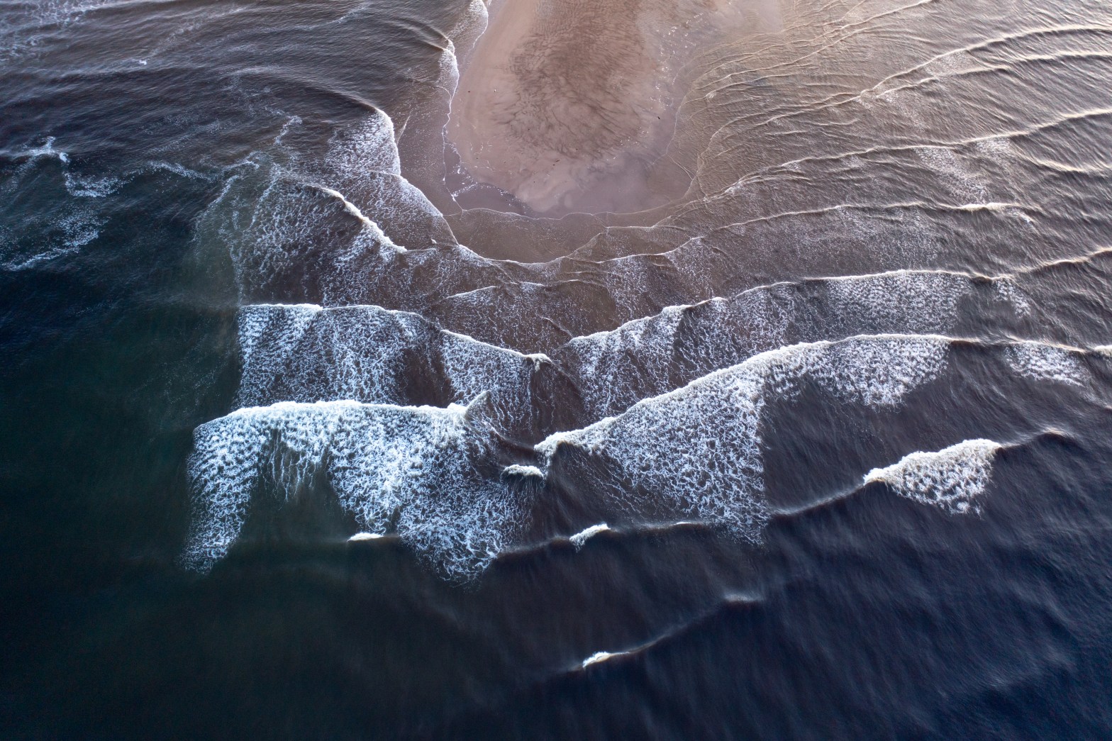 Aerial view of ocean waves gently crashing on a sandy shore.