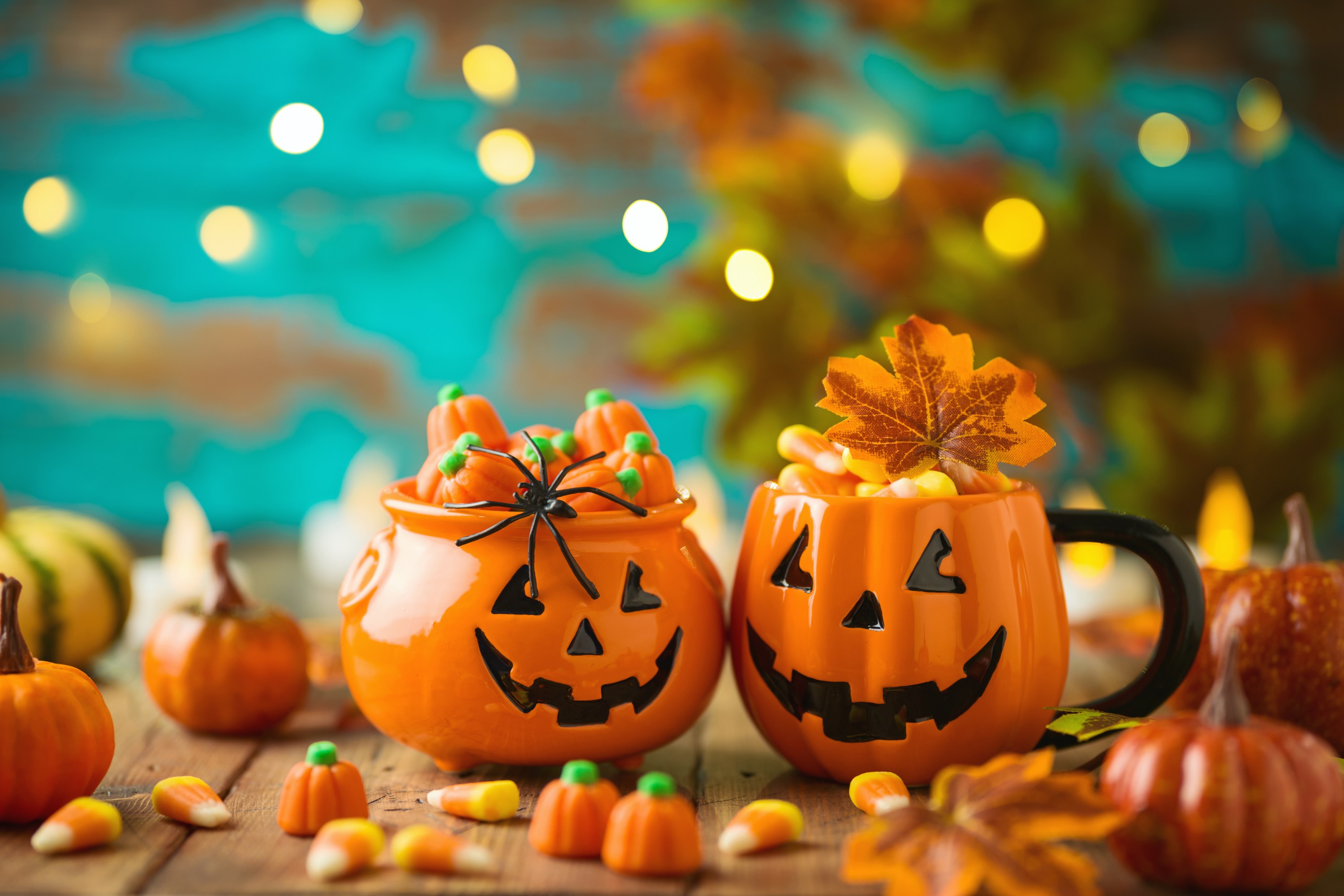 Two pumpkin containers filled with candy corn and pumpkins on a wooden table, with fall decor and lights.